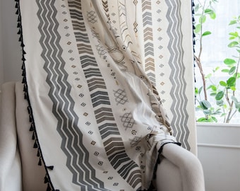 May include: White curtain panel with a black and brown geometric pattern. The curtain has a fringe trim along the bottom edge.