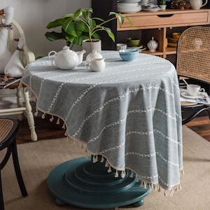 May include: A gray and white striped tablecloth with a fringe border and tassels. The tablecloth is laid on a round table with a teal blue base.
