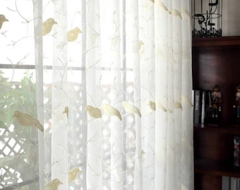 May include: White sheer curtains with embroidered birds and branches. The curtains are hung on a window with a wooden frame.