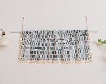 May include: A cream-colored valance with a blue leaf pattern and a fringe trim. The valance is hung on a white rod.