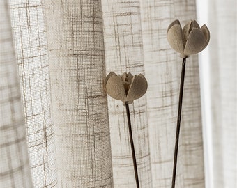 May include: Two dried flower stems with beige flower heads against a backdrop of sheer, white linen curtains with a subtle grid pattern.