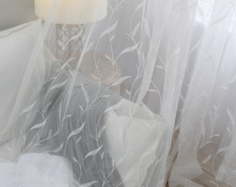 Puede incluir: Cortinas blancas y transparentes con un patrón floral bordado. Las cortinas están colgadas en una habitación con una lámpara y un libro sobre una mesa.
