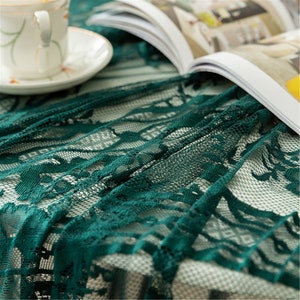 May include: A green lace tablecloth with a delicate floral pattern. The tablecloth is made of a soft, sheer fabric and has a beautiful drape.