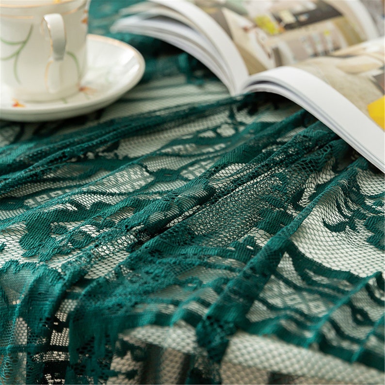 May include: A green lace tablecloth with a delicate floral pattern. The tablecloth is made of a soft, sheer fabric and has a beautiful drape.