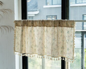 May include: A cream-colored valance with a floral print and tassel trim. The valance is hung on a window with a view of a building in the background.