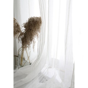 Peut inclure: Rideaux blancs et transparents à rayures verticales. Les rideaux sont suspendus à une fenêtre et laissent passer la lumière naturelle.