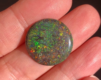 May include: A round, dark green opal cabochon with iridescent flashes of blue, red, and yellow.