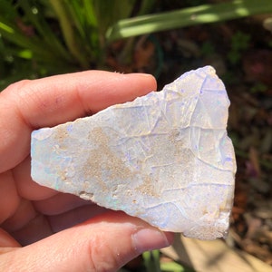 May include: A rough, white opal with iridescent blue and purple flashes. The opal is a natural stone with a rough, irregular shape.