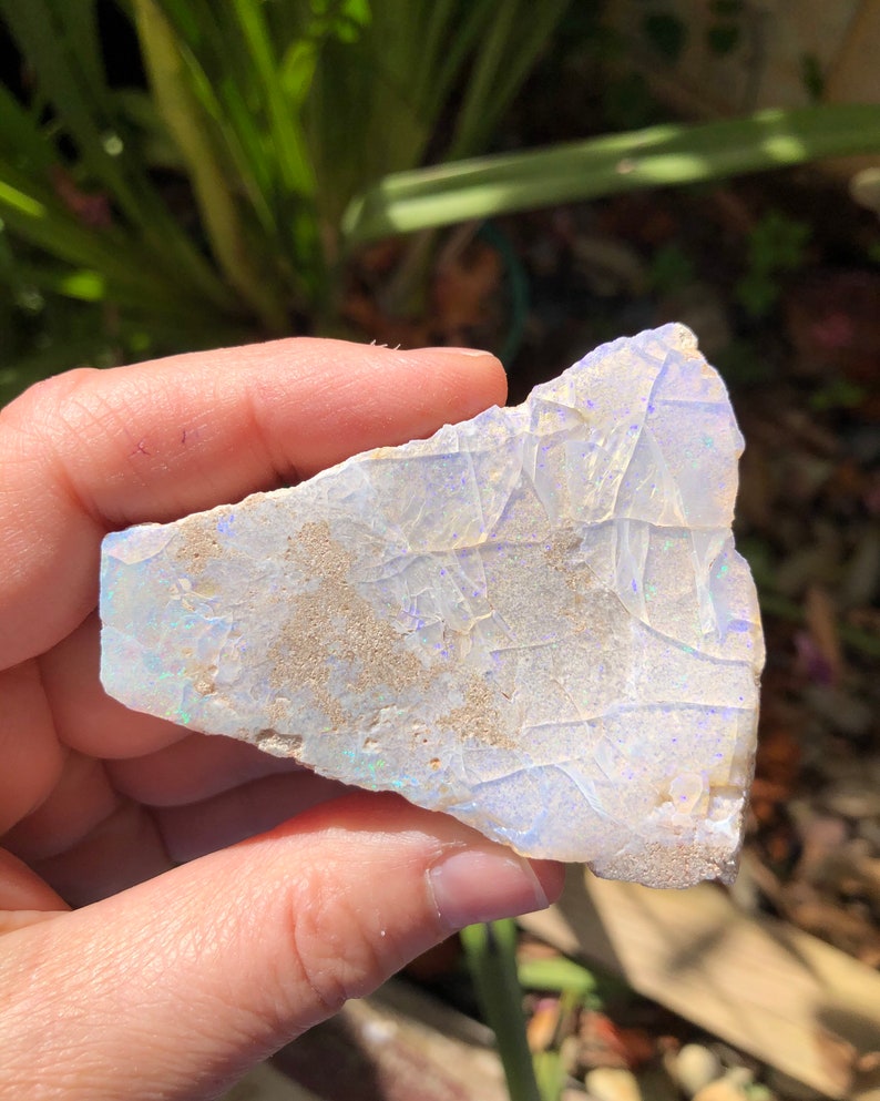May include: A rough, white opal with iridescent blue and purple flashes. The opal is a natural stone with a rough, irregular shape.