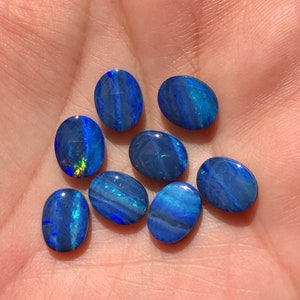 May include: Eight oval-shaped blue opal gemstones with iridescent flashes of colour.