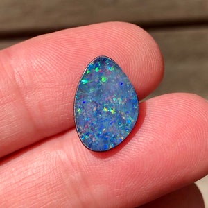 May include: A blue, green and red opal gemstone with a pear shape, set in a silver bezel.
