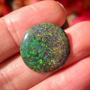 May include: A round, green, black and blue opal gemstone with a speckled pattern.