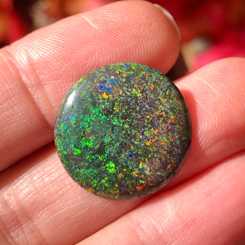 May include: A round, green, black and blue opal gemstone with a speckled pattern.