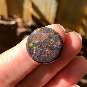 May include: A round, black opal cabochon with a dark brown matrix and flashes of green, red, and blue.