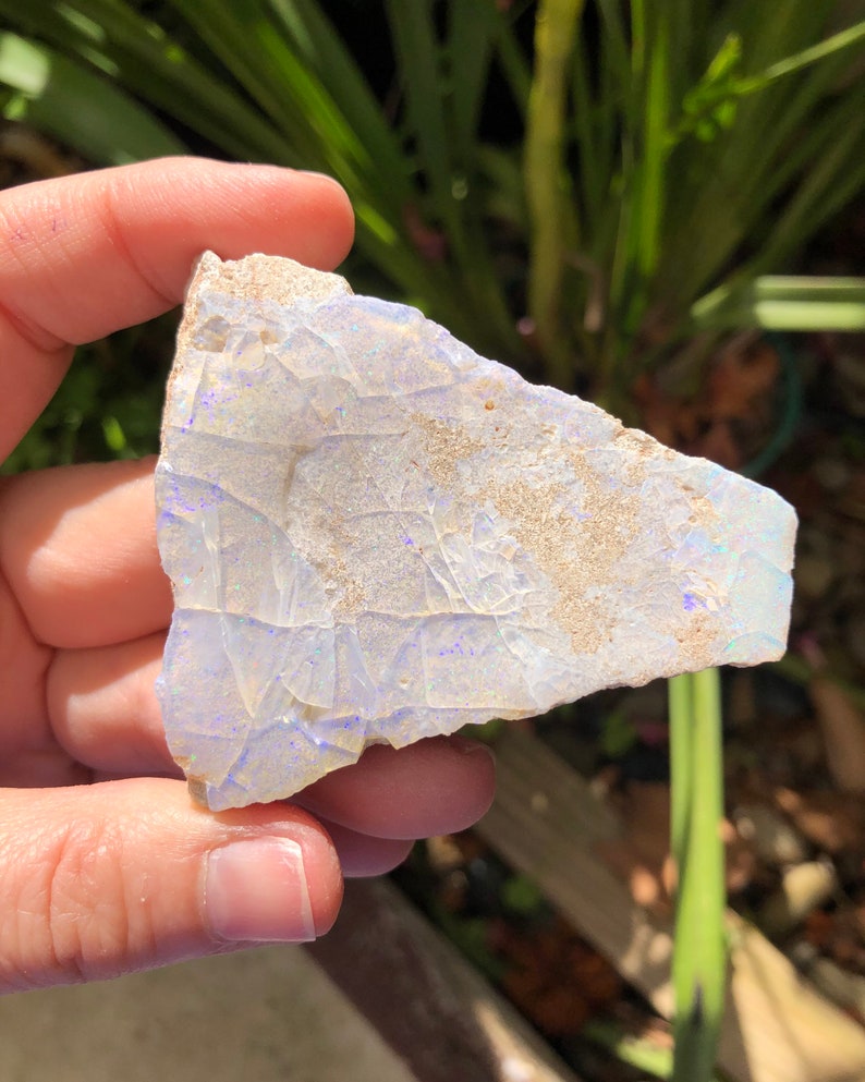 May include: A piece of white opal with blue and purple iridescence. The opal is rough and has a natural, irregular shape.