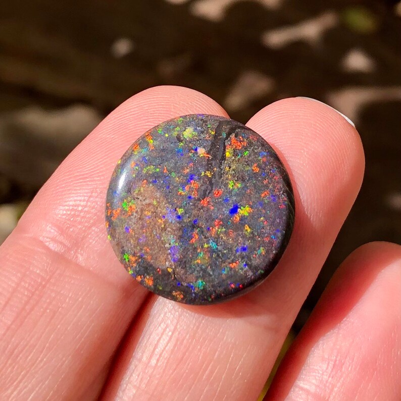 May include: A round, black opal cabochon with a dark, iridescent surface. The opal has a variety of colors, including red, orange, yellow, green, blue, and purple.