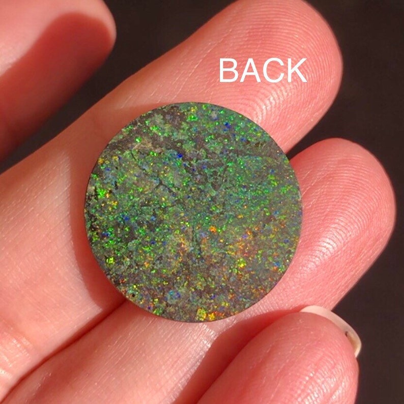 May include: A round, green opal cabochon with a dark, iridescent surface. The back of the opal is visible, showing a dark, green, and brown pattern.
