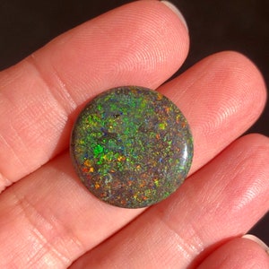 May include: A round, dark green opal cabochon with flashes of red, orange, and blue.