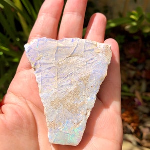 May include: A white and iridescent opal with a rough, natural texture. The opal has a light blue and green iridescence.