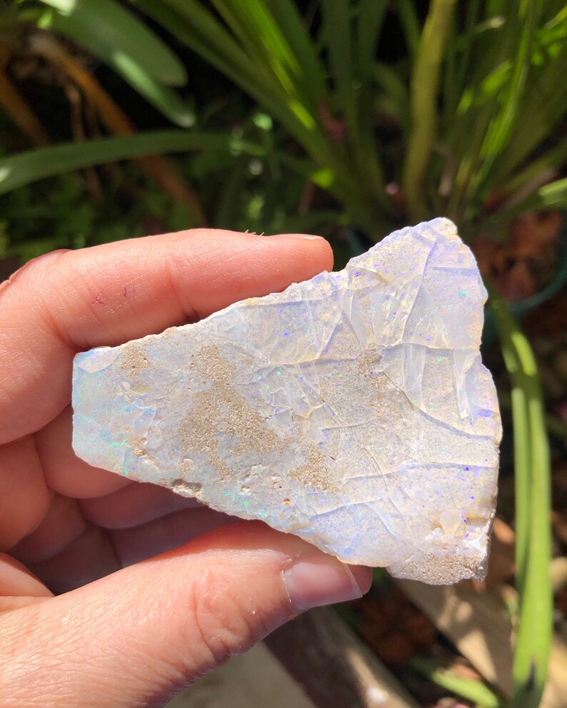 May include: A white opal with iridescent blue and purple flashes. The opal is rough and has a natural, irregular shape.