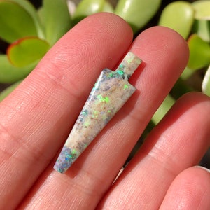 May include: A white, iridescent, arrow-shaped pendant made of opal. The pendant has a light green and blue iridescence.
