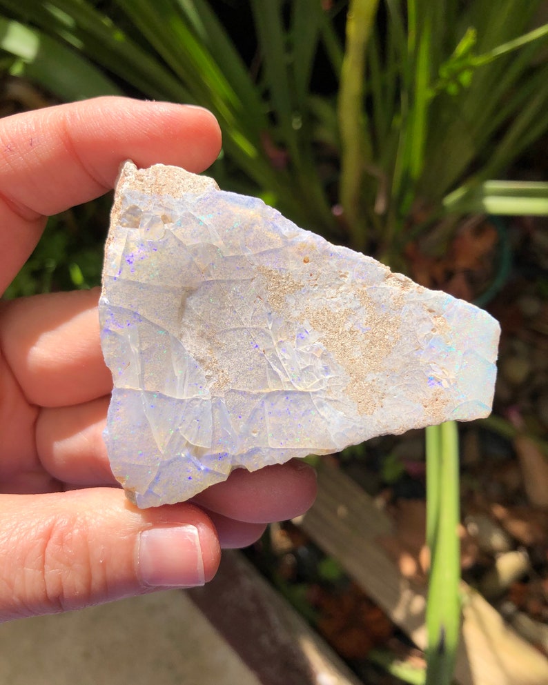 May include: A piece of white opal with blue and purple iridescence. The opal is rough and has a natural, irregular shape.