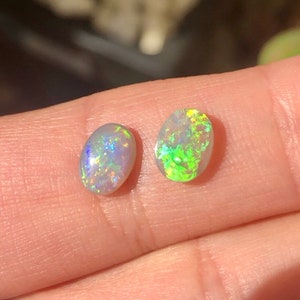 May include: Two oval-shaped opals, one with a green and yellow iridescent sheen and the other with a blue and purple iridescent sheen.
