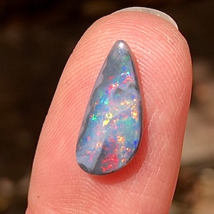 May include: A teardrop-shaped black opal gemstone with iridescent flashes of blue, green, red, and gold.
