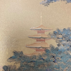 May include: A gold fabric with a detailed image of a pagoda and pine trees. The pagoda is red and white with gold trim. The pine trees are blue and green.
