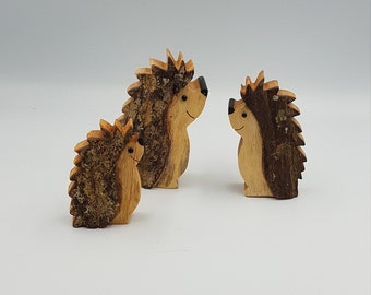 May include: Three wooden hedgehogs of varying sizes, carved from wood with a natural bark texture. The hedgehogs have painted black eyes and a brown and light brown color scheme.