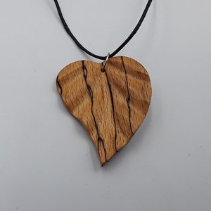 May include: A wooden heart pendant necklace with a black cord. The heart is made of wood with dark brown streaks and a natural wood colour.