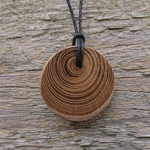 Colgante redondo de madera elaborado con Laburnum y colgado en una correa ajustable de algodón encerado.