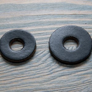 May include: Two black leather rings with a hole in the centre. The rings are on a light wood surface.
