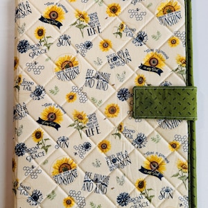 May include: Quilted fabric binder with a sunflower and bee pattern. The cover features yellow sunflowers, blue floral accents, and inspirational phrases like "Create Your Own Sunshine" and "Bee Humble and Kind." The binder has a green border and a green tab closure.