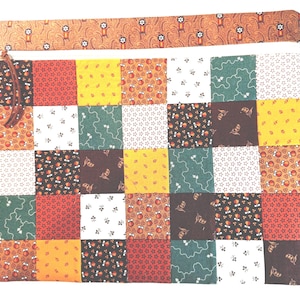 May include: A square zippered pouch featuring a patchwork design of various fabric squares in shades of red, yellow, green, brown, and white. The patterns include floral, star, and geometric motifs. A brown leather pull is attached to the zipper.