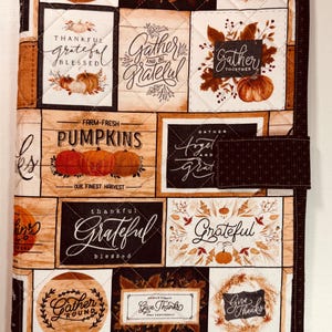 May include: A quilted fabric cover featuring a patchwork design of autumn-themed rectangular panels. The print includes illustrations of pumpkins, fall foliage, and text such as "Gather," "Grateful," "Farm-Fresh Pumpkins," and "Give Thanks."