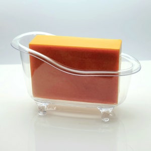 May include: A clear plastic bathtub-shaped soap dish with a rectangular bar of orange soap inside.