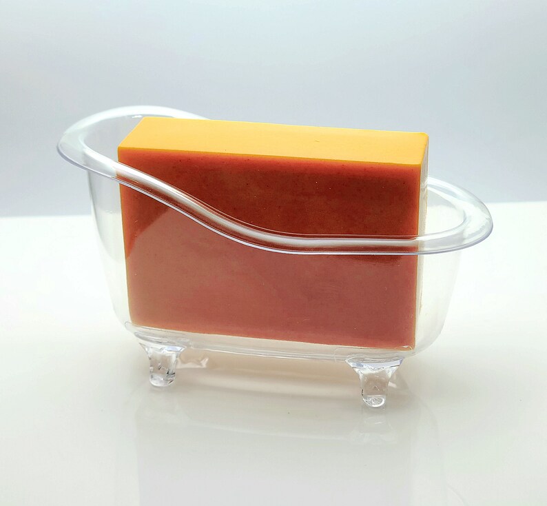 May include: A clear plastic bathtub-shaped soap dish with a rectangular bar of orange soap inside.