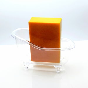 May include: A clear plastic bathtub-shaped soap dish with a bright yellow bar of soap inside.