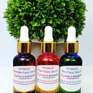 May include: Three glass bottles with gold lids and droppers containing face serums. The bottles are labeled "All Natural Lavender Face Serum", "All Natural Rose Face Serum", and "All Natural Mint Face Serum". Each bottle has a label with the company name "NANA'S NATURALS" and the phrase "Products Made with Love".