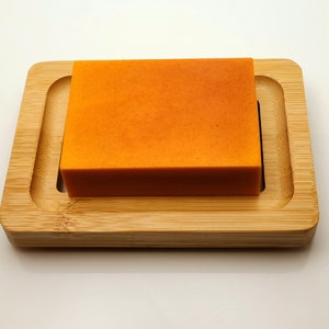 May include: A bright orange bar of soap resting on a wooden soap dish.