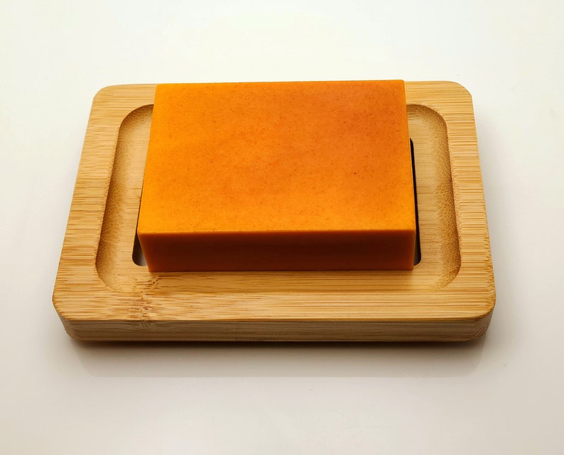 May include: A bright orange bar of soap resting on a wooden soap dish.