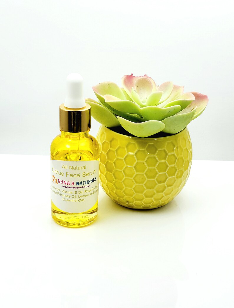 May include: A glass bottle of all-natural citrus face serum with a gold lid and dropper. The bottle is sitting on a white surface next to a yellow planter with a green succulent.