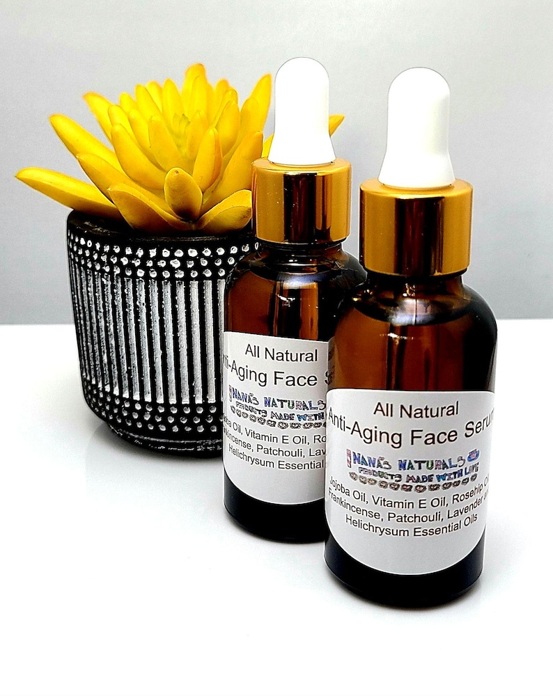 May include: Two amber glass bottles with gold lids and white droppers filled with a brown liquid. The bottles are labeled "All Natural Anti-Aging Face Serum" and feature the text "NANA'S NATURALS MADE WITH LOVE". The bottles are sitting on a white surface.