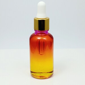 May include: A glass bottle with a gold lid and a white dropper. The bottle is filled with a liquid that is a gradient of orange and yellow.