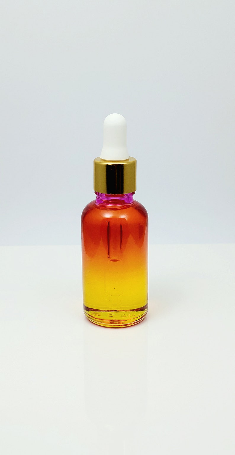 May include: A glass bottle with a gold lid and a white dropper. The bottle is filled with a liquid that is a gradient of orange and yellow.