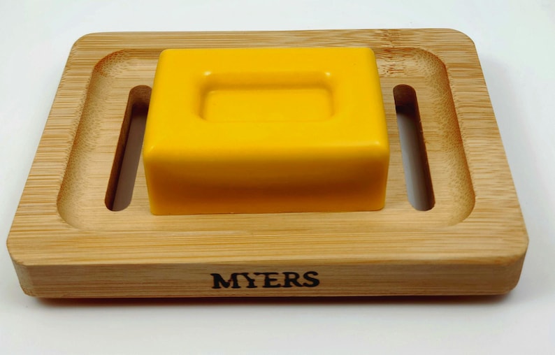 May include: A yellow bar of soap sits on a wooden soap dish with the word "MYERS" printed on the front.