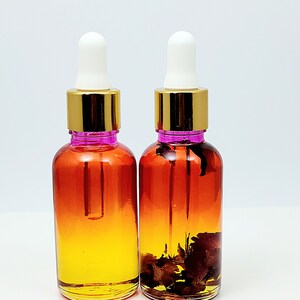 May include: Two amber glass bottles with gold lids and white droppers. The bottles are filled with a yellow liquid and contain dried flower petals.