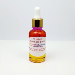 May include: A clear glass bottle with a gold lid and a dropper top. The bottle is filled with a yellow liquid and has a white label that reads "All Natural Rose Face Serum Nana's Naturals Products Made with Love Jojoba Oil, Vitamin E Oil, Rosehip Oil, Rose and Jasmine Essential Oils".