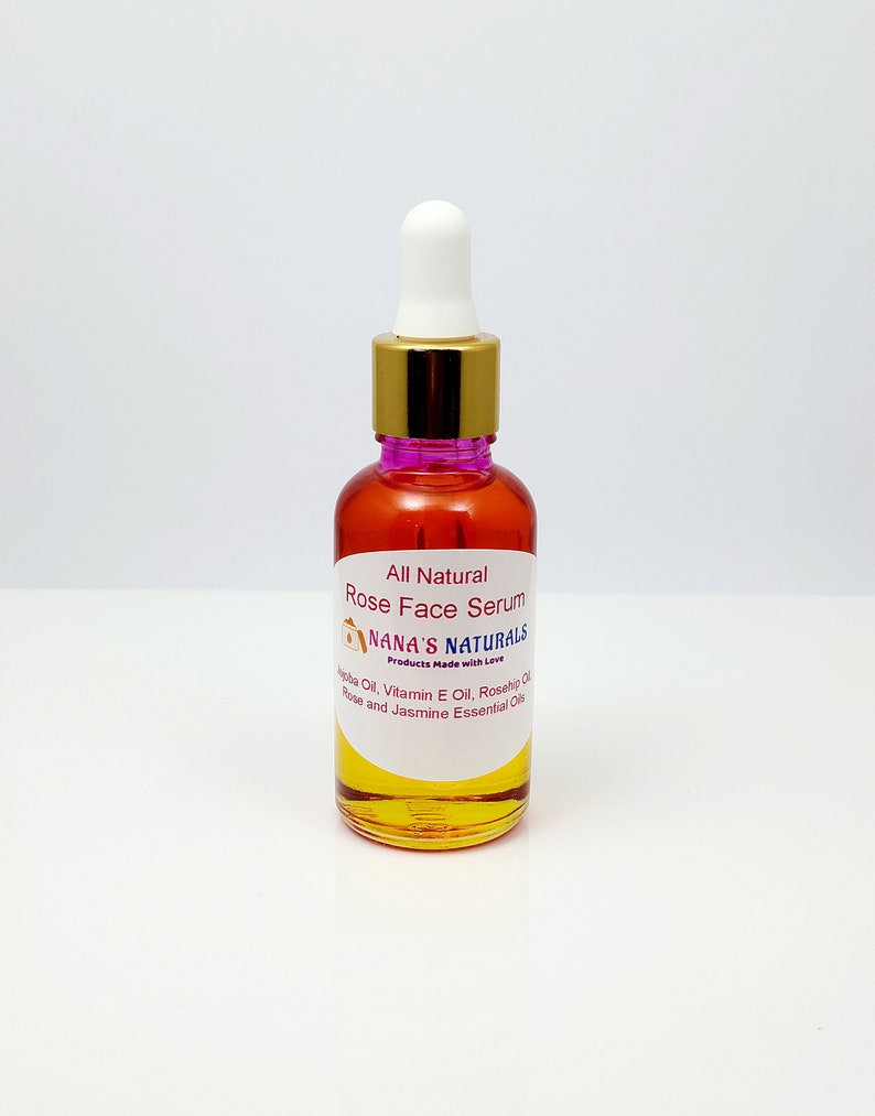 May include: A clear glass bottle with a gold lid and a dropper top. The bottle is filled with a yellow liquid and has a white label that reads "All Natural Rose Face Serum Nana's Naturals Products Made with Love Jojoba Oil, Vitamin E Oil, Rosehip Oil, Rose and Jasmine Essential Oils".